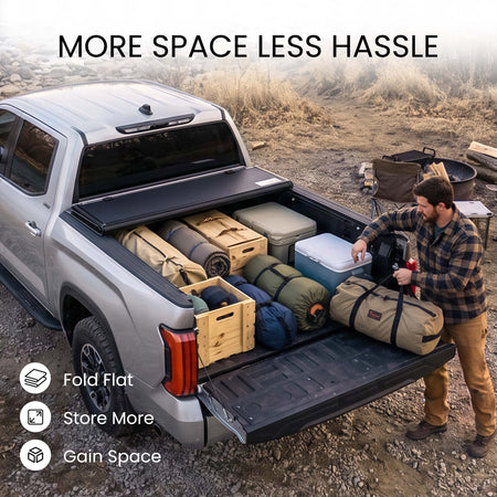 Folding truck bed cover propped open with firewood, skis, and duffels loaded in a pickup bed