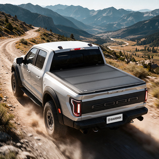 Ford F-150 with a hard bed cover speeding on a gravel mountain road, dust trailing behind