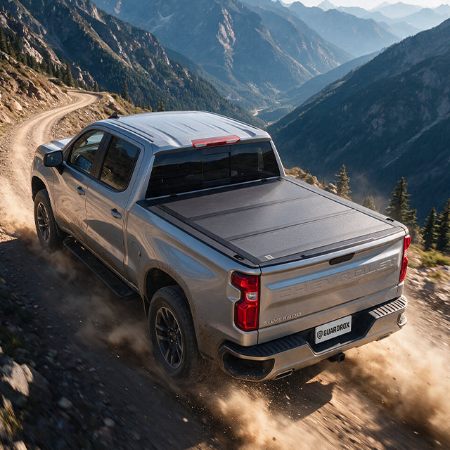 Chevy Silverado with a hard bed cover speeding on a gravel mountain road, dust trailing behind