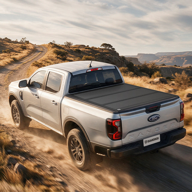 Ford Ranger with a hard bed cover speeding on a gravel mountain road, dust trailing behind