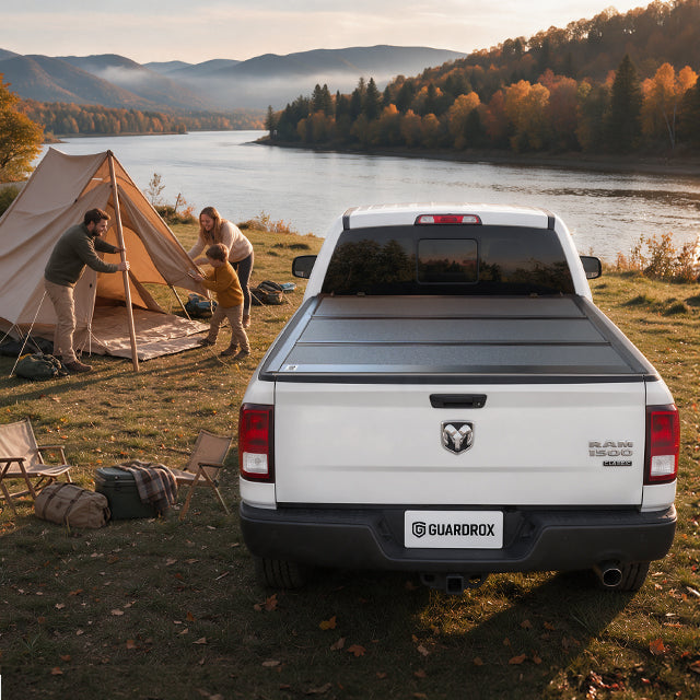 Family unpacking camping gear from an open Dodge RAM 1500 Classic bed beside a lakeside campsite in autumn